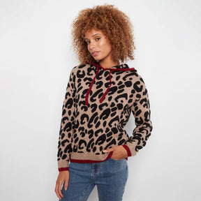 A woman with curly brown hair wearing a beige and black leopard print hoodie with dark red trim and drawstrings, paired with blue jeans, against a plain white background.