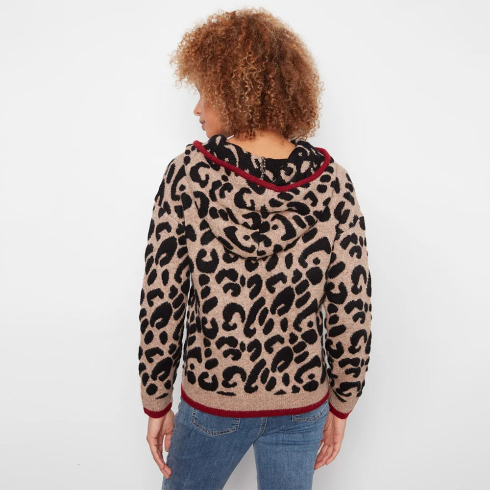 A woman with curly light brown hair is shown from the back wearing a beige and black leopard print hooded sweater with red trim, paired with blue jeans, against a plain white background.
