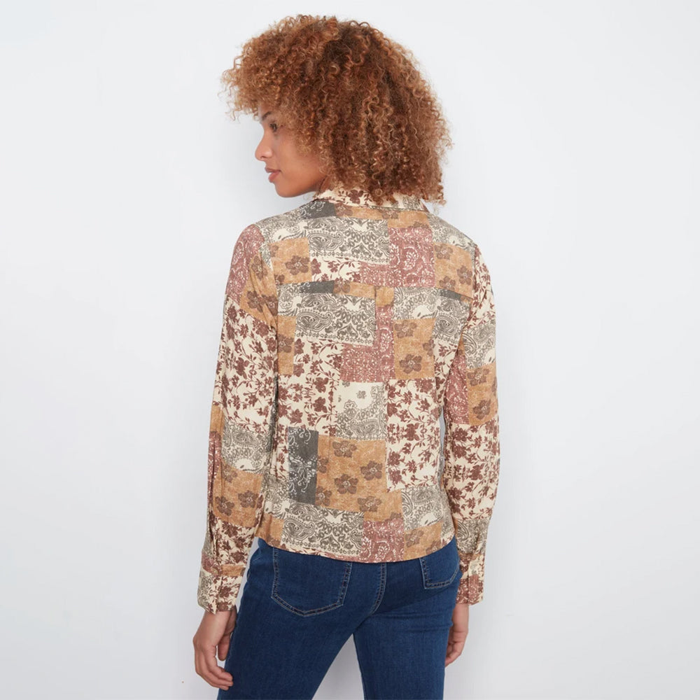 A woman with curly auburn hair is shown from the back wearing a long-sleeve button-up shirt with a multicolor patchwork floral and paisley print, paired with blue jeans, against a plain white background.