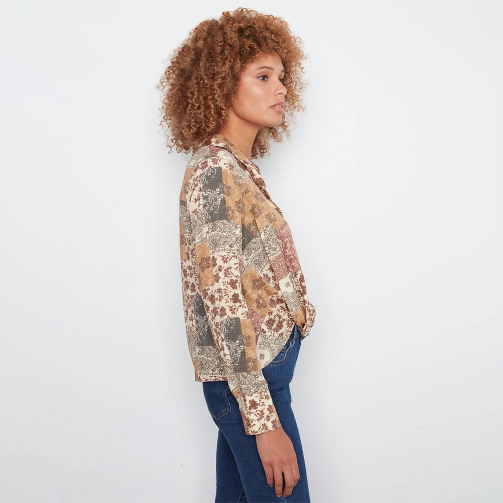 A woman with curly light brown hair is shown in profile wearing a long-sleeve button-up shirt with a vintage patchwork floral pattern in beige, brown, and muted red, paired with blue jeans, against a plain white background.