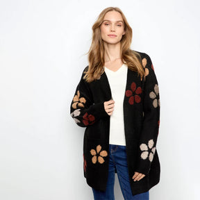 A woman modeling a black open-front cardigan with large multicolor floral motifs in red, beige, and brown, worn over a white top and blue jeans against a plain white background.