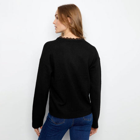 A woman shown from the back wearing a black long-sleeve sweater with a decorative brown lace trim at the crew neck, paired with blue jeans, against a plain white background.