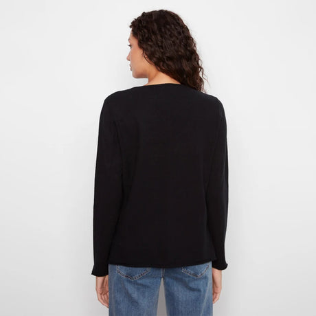 A woman with curly dark hair is shown from the back wearing a black long-sleeve knit top and blue jeans against a plain white studio background.