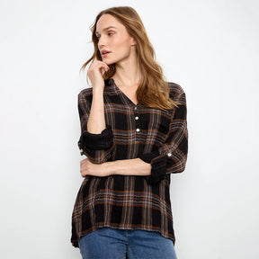 A woman modeling a black long-sleeve plaid button-up shirt with brown and orange stripes, paired with blue jeans, against a plain white studio background.