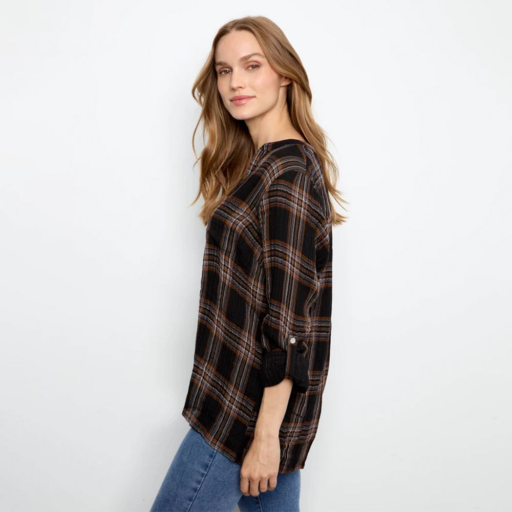 A woman modeling a black plaid button-up shirt with brown and orange stripes, paired with blue jeans, against a plain white background.