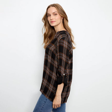 A woman modeling a black plaid button-up shirt with brown and orange stripes, paired with blue jeans, against a plain white background.
