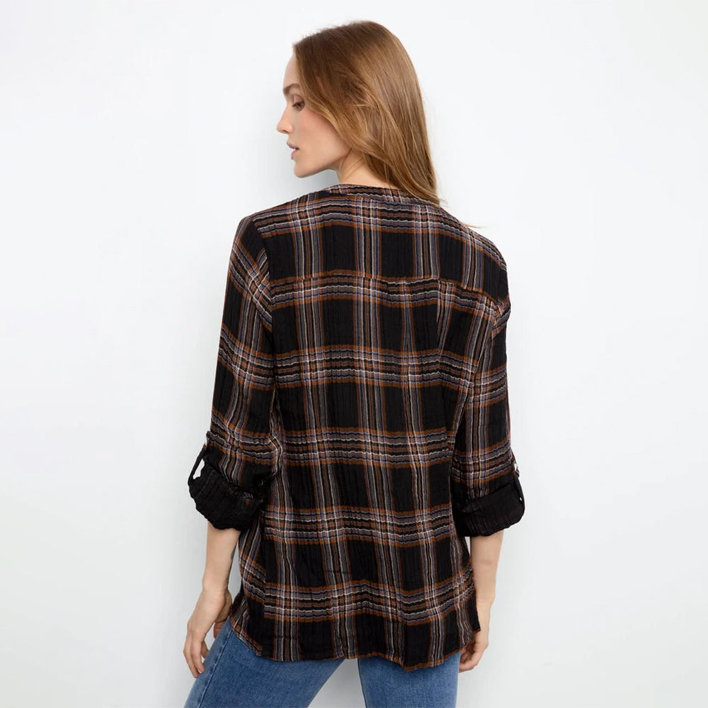 A woman shown from the back wearing a black plaid button-up shirt with rolled-up sleeves and blue jeans, set against a plain white studio background.