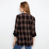 A woman shown from the back wearing a black plaid button-up shirt with rolled-up sleeves and blue jeans, set against a plain white studio background.