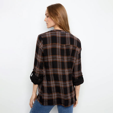 A woman shown from the back wearing a black plaid button-up shirt with rolled-up sleeves and blue jeans, set against a plain white studio background.