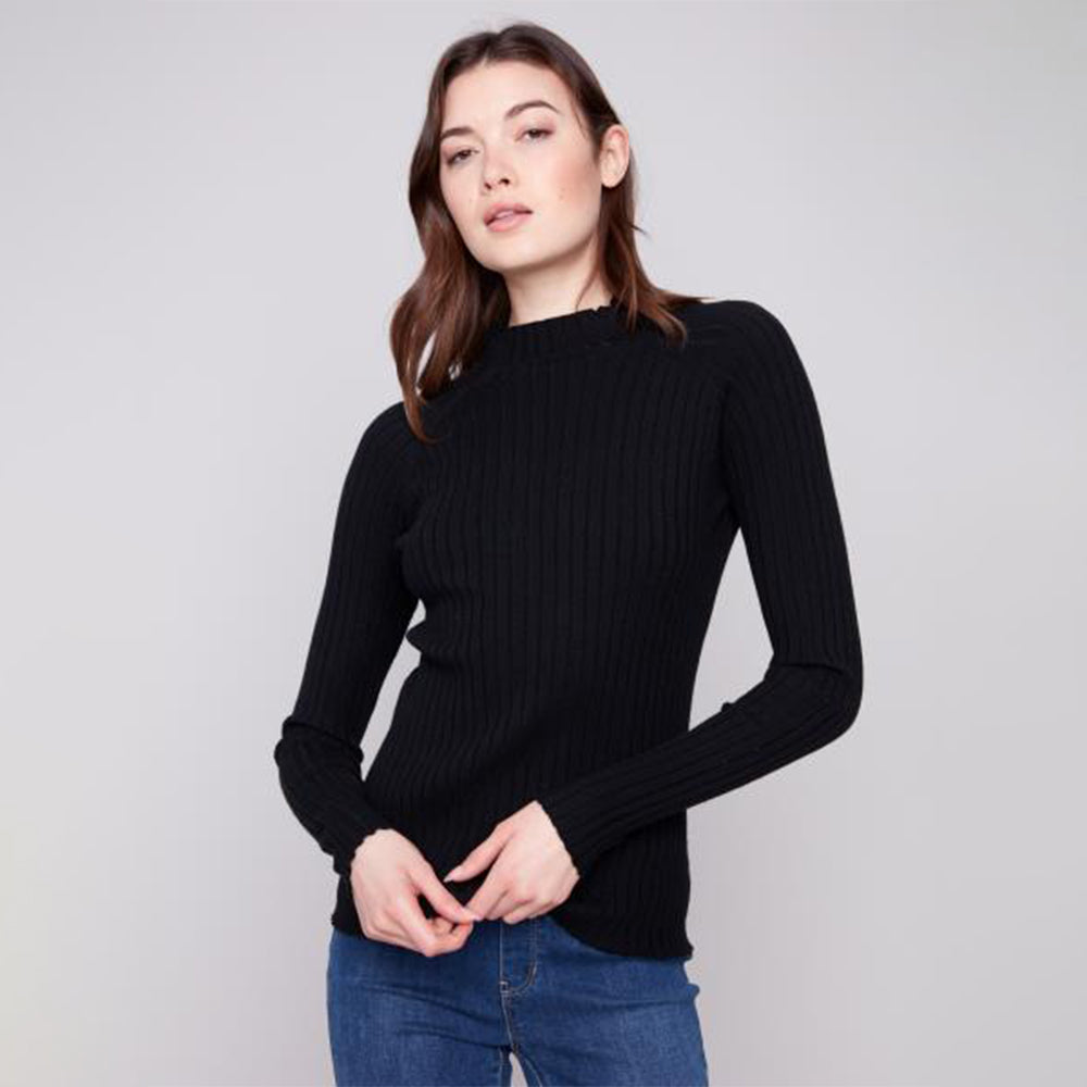 Woman wearing a black ribbed sweater and blue jeans on a light gray background