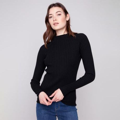 Woman wearing a black ribbed sweater and blue jeans on a light gray background