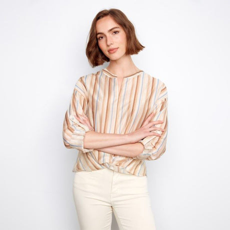 Woman wearing a striped shirt and white pants against a plain background