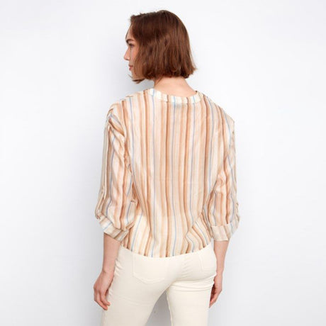 Woman wearing a striped shirt and white pants against a plain background