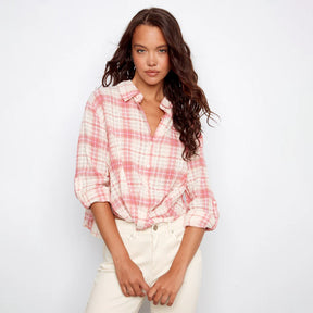 Woman wearing a pink and white plaid shirt with rolled-up sleeves on a plain background