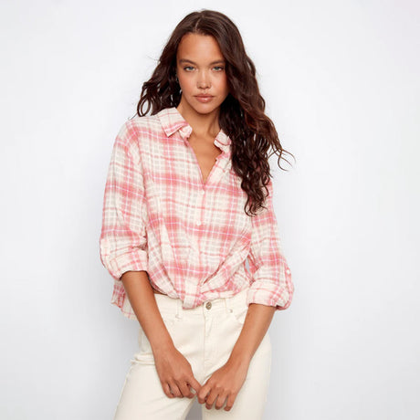 Woman wearing a pink and white plaid shirt with rolled-up sleeves on a plain background