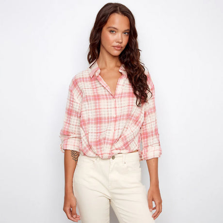 Woman wearing a pink plaid shirt and white pants on a plain background