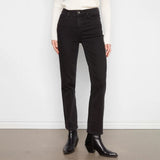 A person wearing black straight-leg jeans, a white ribbed sweater, and black ankle boots, standing against a white wall and gray floor.