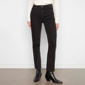 A person wearing black straight-leg jeans, a white ribbed sweater, and black ankle boots, standing against a white wall and gray floor.