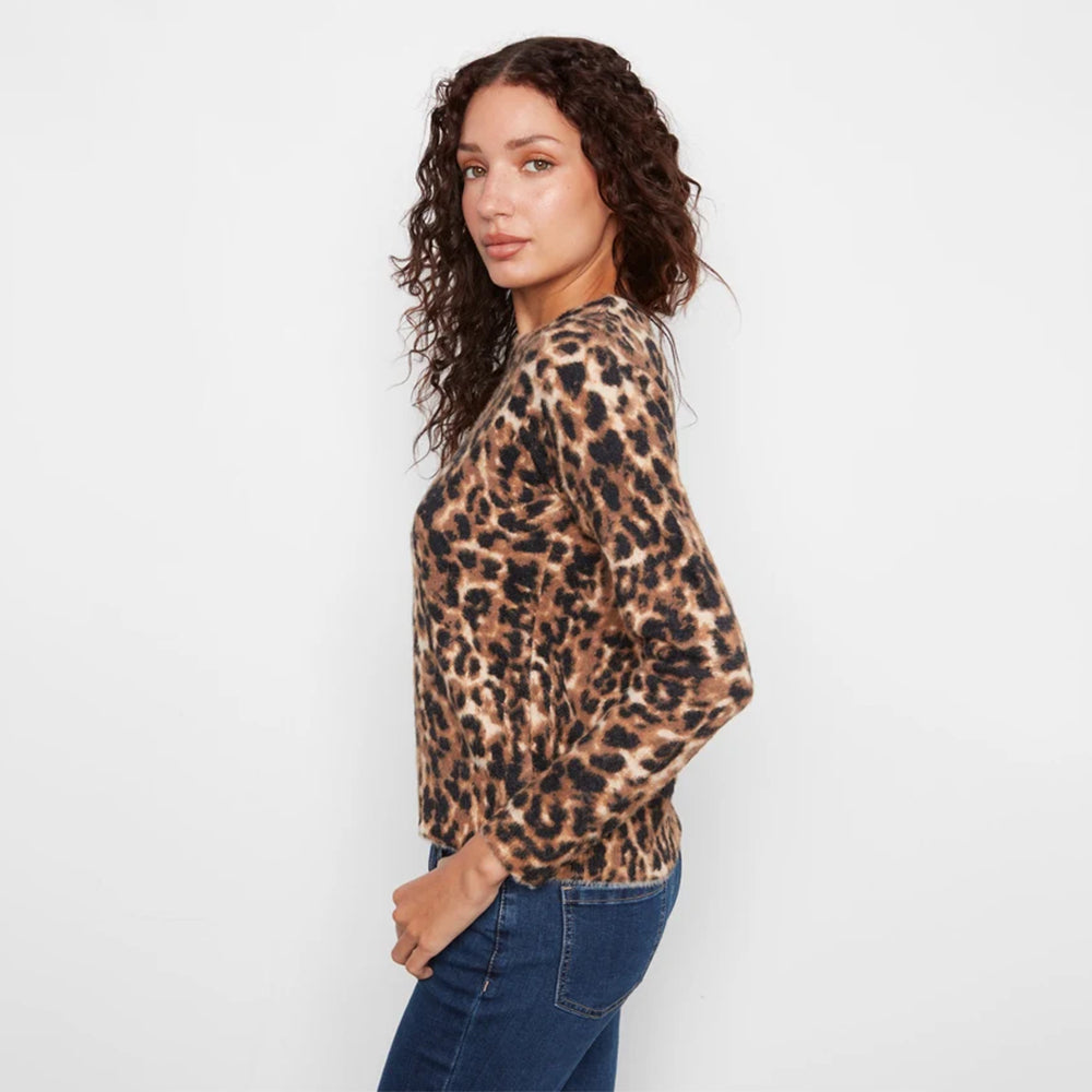 A woman with curly brown hair is shown from a side-back angle wearing a long-sleeve leopard print sweater and blue jeans against a plain white studio background.