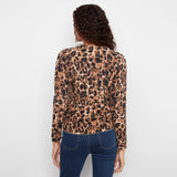 A woman viewed from the back wearing a leopard-print long-sleeve top and blue jeans against a plain white background.
