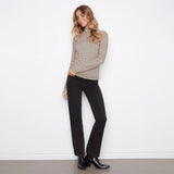A woman modeling a beige and black checkered long-sleeve mock neck sweater, paired with black jeans and black leather ankle boots, standing against a white wall.