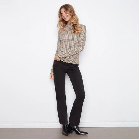 A woman modeling a beige and black checkered long-sleeve mock neck sweater, paired with black jeans and black leather ankle boots, standing against a white wall.