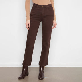 A model wearing dark brown straight-leg jeans, a beige long-sleeve top, and dark brown leather ankle boots, standing against a white wall.