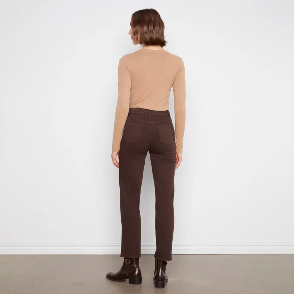 A model shown from the back wearing a beige long-sleeve top, dark brown straight-leg jeans, and dark brown ankle boots, standing against a white wall.
