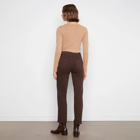 A model shown from the back wearing a beige long-sleeve top, dark brown straight-leg jeans, and dark brown ankle boots, standing against a white wall.