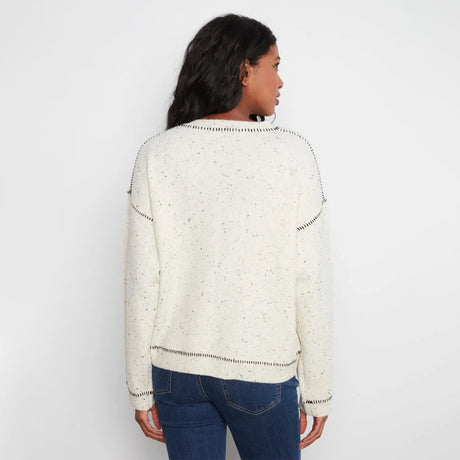 A woman viewed from the back wearing a cream-colored knit sweater with small black speckles and black dotted trim details, paired with blue jeans, against a plain white background.