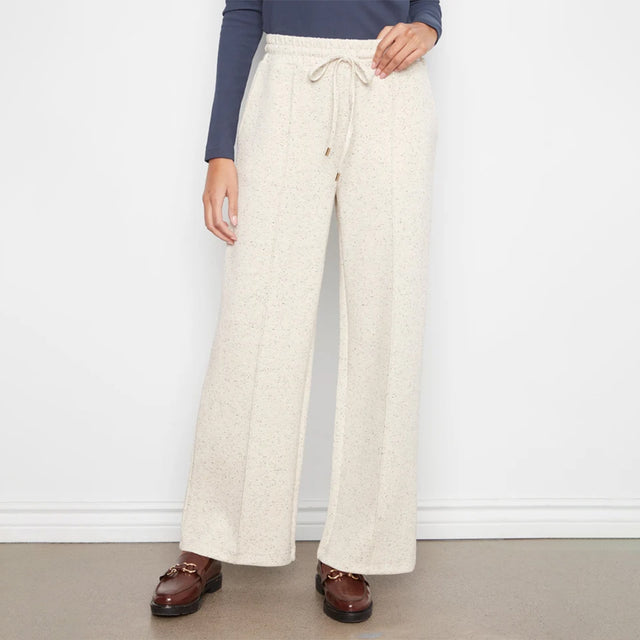 A person wearing cream-colored wide-leg knit pants with a drawstring waist, paired with a navy long-sleeve top and brown loafers, standing against a white wall.