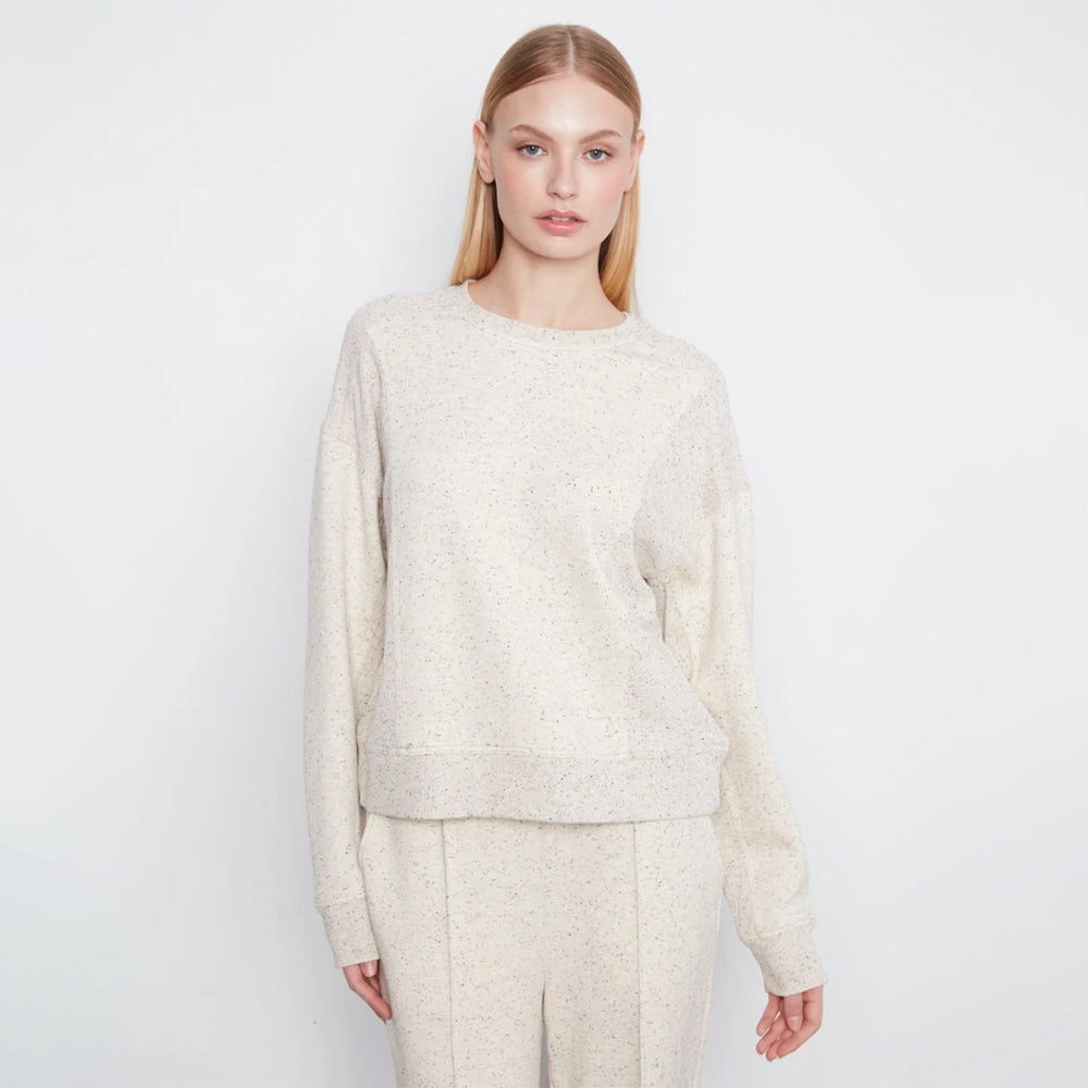 A woman modeling a cream-colored, textured knit crewneck sweater and matching trousers against a plain white studio background.