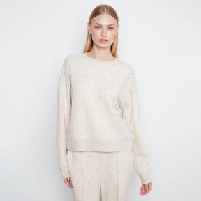 A woman modeling a cream-colored, textured knit crewneck sweater and matching trousers against a plain white studio background.