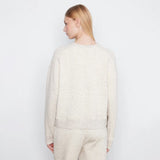 A woman shown from the back wearing a cream-colored, textured knit crewneck sweater and matching knit pants against a plain white studio background.