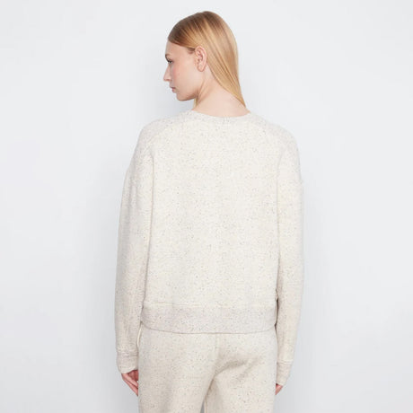 A woman shown from the back wearing a cream-colored, textured knit crewneck sweater and matching knit pants against a plain white studio background.