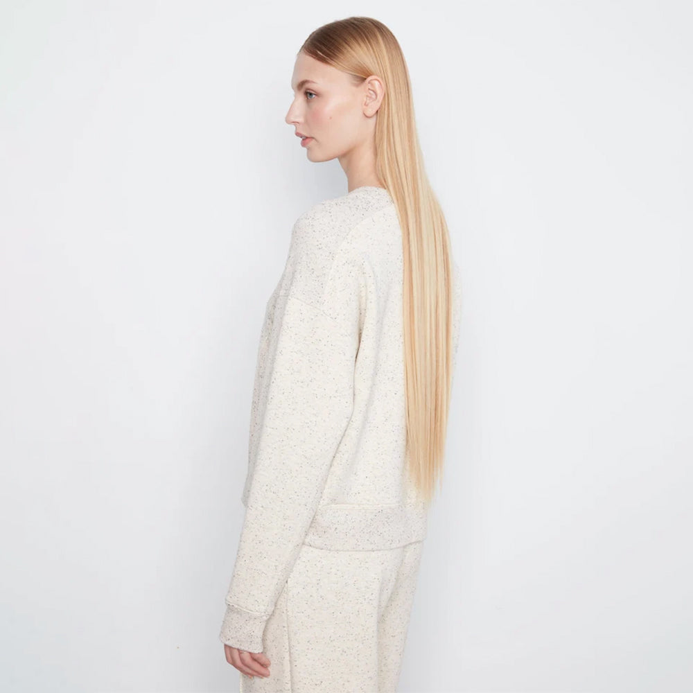 A woman with long blonde hair is shown in profile wearing a textured cream knit sweater and matching knit pants against a plain white studio background.