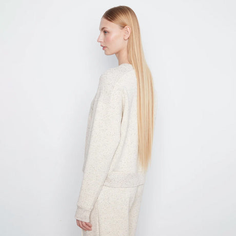 A woman with long blonde hair is shown in profile wearing a textured cream knit sweater and matching knit pants against a plain white studio background.