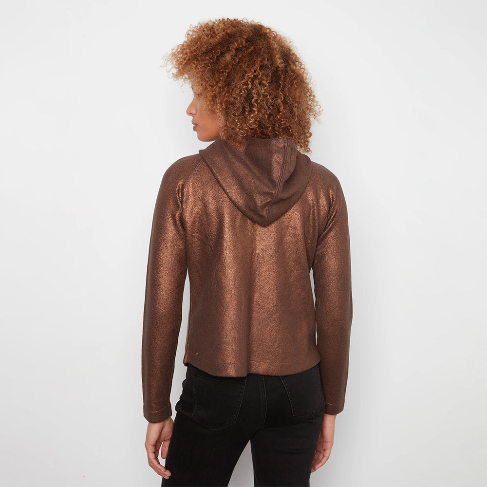 A woman with curly brown hair is shown from the back wearing a metallic bronze cropped hoodie and black jeans against a plain white background.