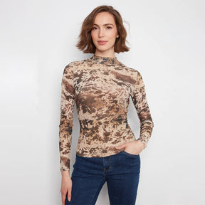 A woman modeling a fitted long-sleeve mock neck top with an abstract brown and beige pattern, paired with dark blue jeans, against a plain light gray background.