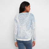 A woman viewed from the back wearing a light blue and white patterned knit sweater with blue jeans, set against a plain white studio background.