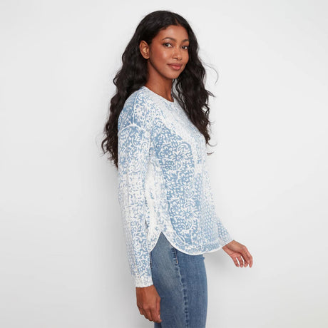 A woman modeling a light blue and white patterned long-sleeve top with blue jeans, standing against a plain white studio background.