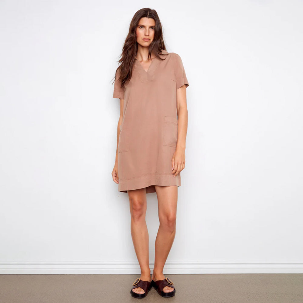 Woman wearing a beige dress standing against a white wall