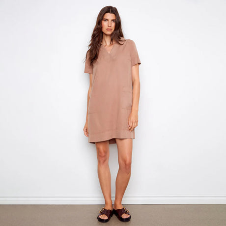 Woman wearing a beige dress standing against a white wall