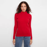 A woman modeling a bright red ribbed mock neck long-sleeve sweater paired with blue jeans, set against a plain white studio background.