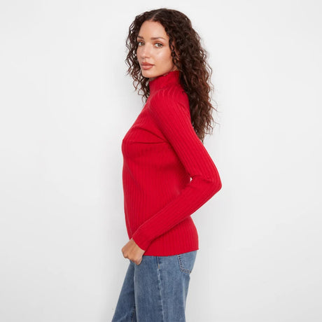 A woman with long, curly brown hair is shown from a side-back angle wearing a bright red ribbed turtleneck sweater and blue jeans against a plain white studio background.
