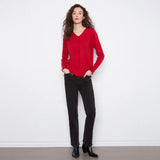 A woman modeling a red long-sleeve V-neck knit sweater paired with black pants and black ankle boots, standing against a plain white wall.