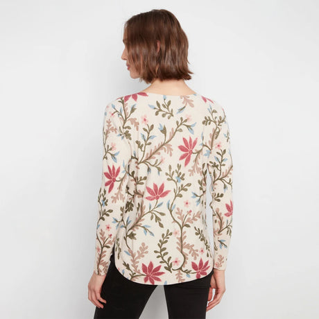 A woman viewed from the back wearing a long-sleeve cream blouse with a pink, green, and blue floral vine pattern, paired with black pants, against a plain white background.