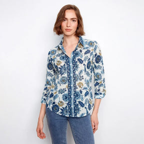 A woman modeling a long-sleeve button-up shirt with a blue and gold floral pattern on a white background, paired with blue jeans, against a plain white studio background.