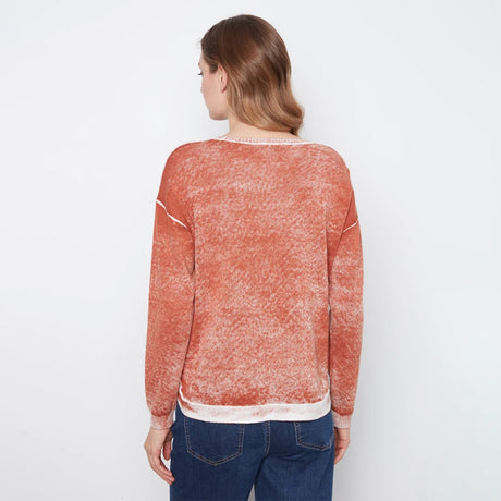 A woman viewed from the back wearing a textured, washed terracotta orange long-sleeve sweater with white contrast trim, paired with blue jeans, against a plain white background.