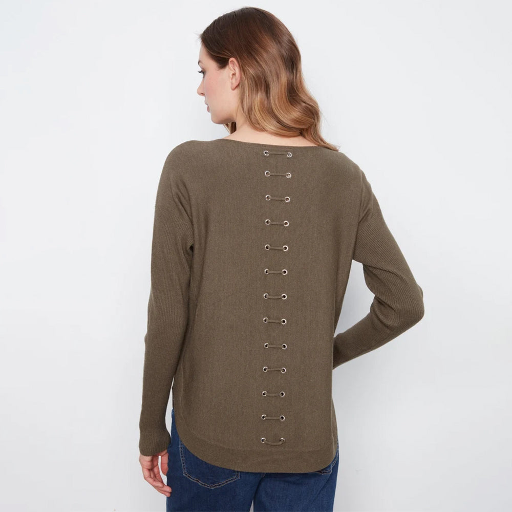 A woman shown from the back wearing a long-sleeve knit top in a muted taupe-brown color, featuring a vertical row of metal eyelets with laces down the back. She is wearing blue jeans against a plain white studio background.